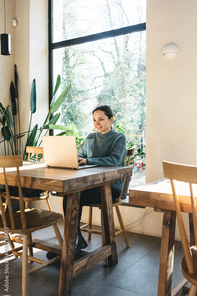 Fototapeta premium A beautiful young girl student or freelancer uses a laptop. She is studying or working remotely.