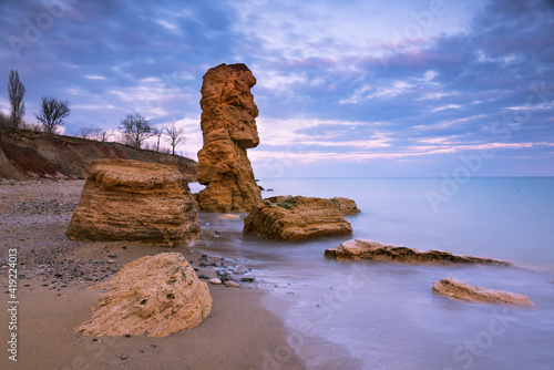 Beautiful seascape with shell rocks on the coast at sunset. One big stone like statue from Easter Island. Long exposure