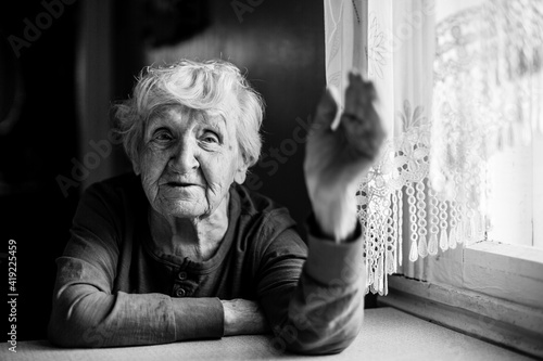 An old woman emotionally talking sitting at a table at the home. Black and white photo.