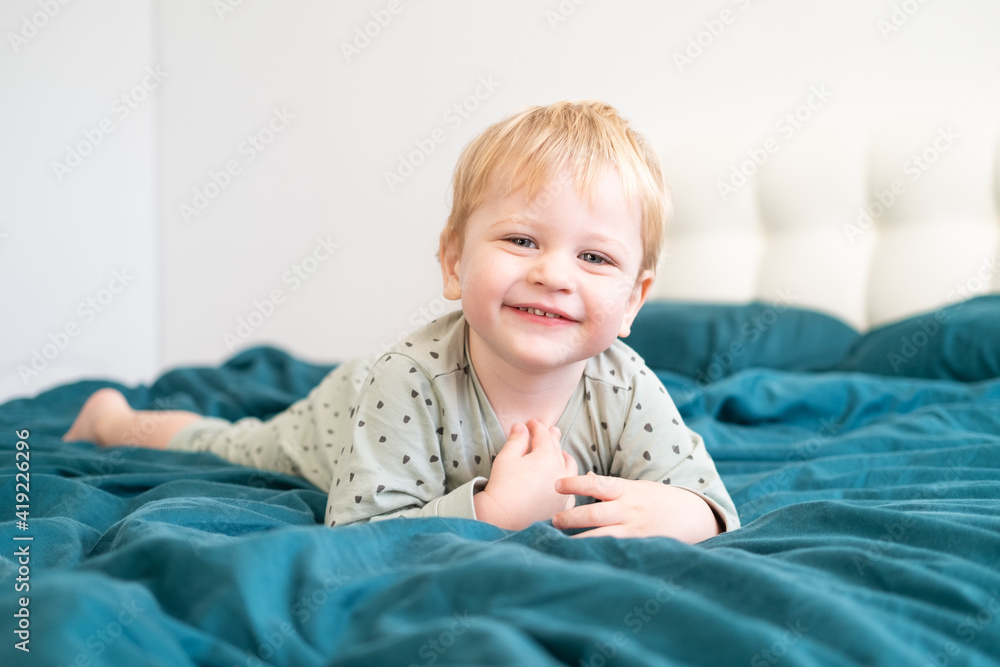 Little healthy toddler boy in green pajamas having fun lying in bed at home Little healthy toddler boy in green pajamas having fun lying in bed at home