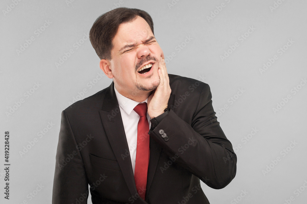 Bad feelings concept. Businessman have toothy dental pain. Indoor, studio shot, isolated on gray background Bad feelings concept. Businessman have toothy dental pain. Indoor, studio shot, isolated on gray background