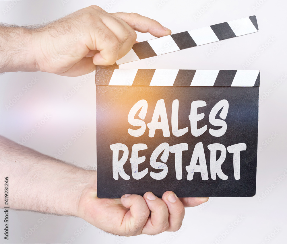 Obraz premium On a white background, a man holds a clapperboard in his hands on which it is written - SALES RESTART