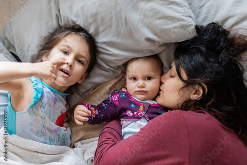 Mother and her two young daughters lying down in bed