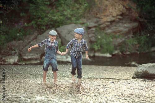 two little brothers in denim overalls and a plaid shirt and caps jump in the water and enjoy