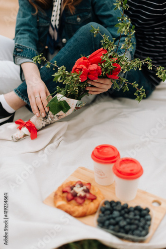 girl with a bouquet of flowers sits on a white plaid, summer picnic