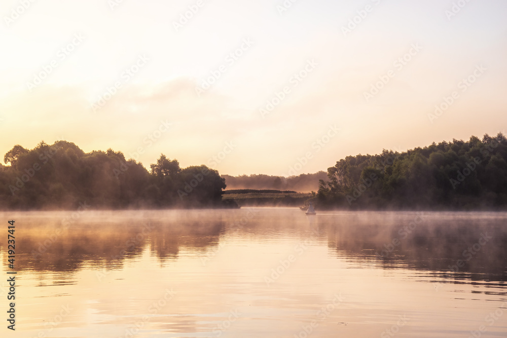 Beautiful countryside morning foggy morning scenery on river with tranquil mirror water and reflections during sunrise in warm colors during golden hour