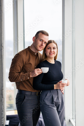 Stylish young couple in love in front of large panoramic windows. Young woman and man stand near a large window