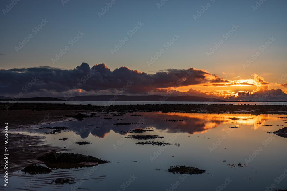 Landscape with sunset over calm ocean, some dreamy purple, orange clouds and mirror like reflection in water