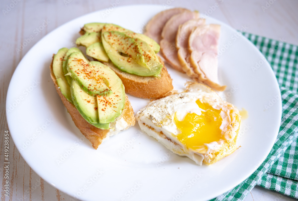 Home cooking breakfast with avocado toast, fried egg and ham on white plate
