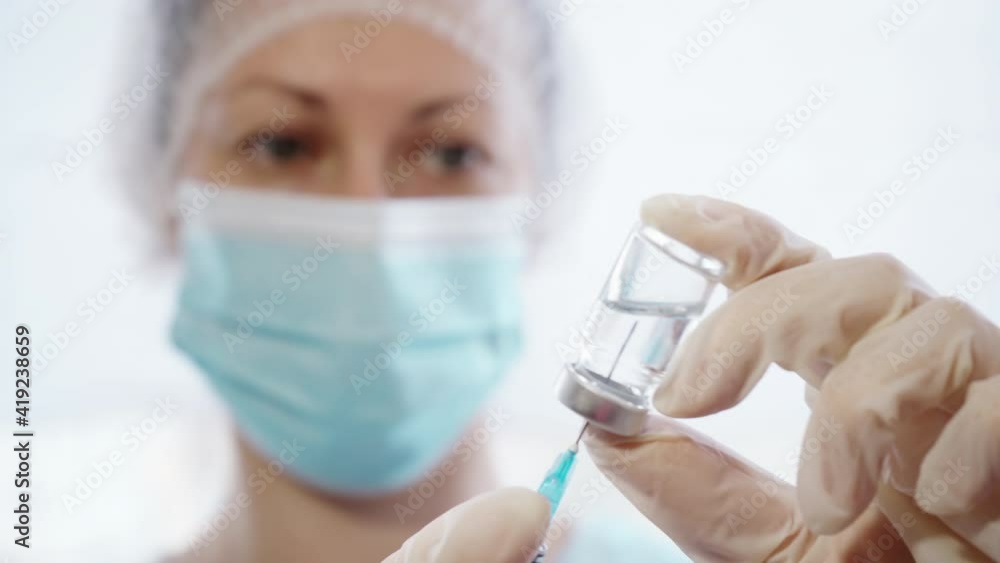Doctor Wearing Medical Mask And Gloves Picking Medicine Into Syringe From Glass Vial. Female Doctor Prepares Solution for Injection Doctor Wearing Medical Mask And Gloves Picking Medicine Into Syringe From Glass Vial. Female Doctor Prepares Solution for Injection