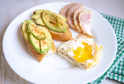 Home cooking breakfast with avocado toast, fried egg and ham on white plate