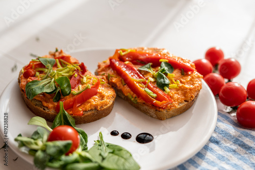 vegan roasted red pepper dip sandwich spread on freshly baked bread slice with salad garnish on white porcelain plate 