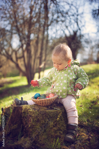 Little girl collects Easter colored eggs during Egg hunt in Spring. Beautiful spring season day. Happy Easter day