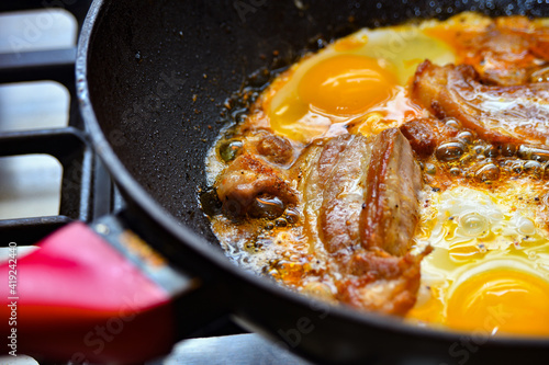 Fried meat with eggs is cooked in a pan, pork steak and chicken eggs.