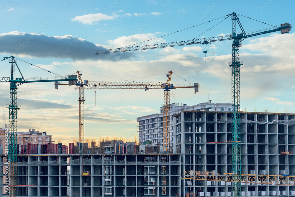 Construction site, cranes and multi-storey unfinished buildings at sunrise or sunset Construction site, cranes and multi-storey unfinished buildings at sunrise or sunset