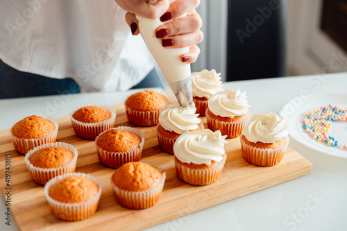 Foto Woman decorates freshly baked cupcakes with cream