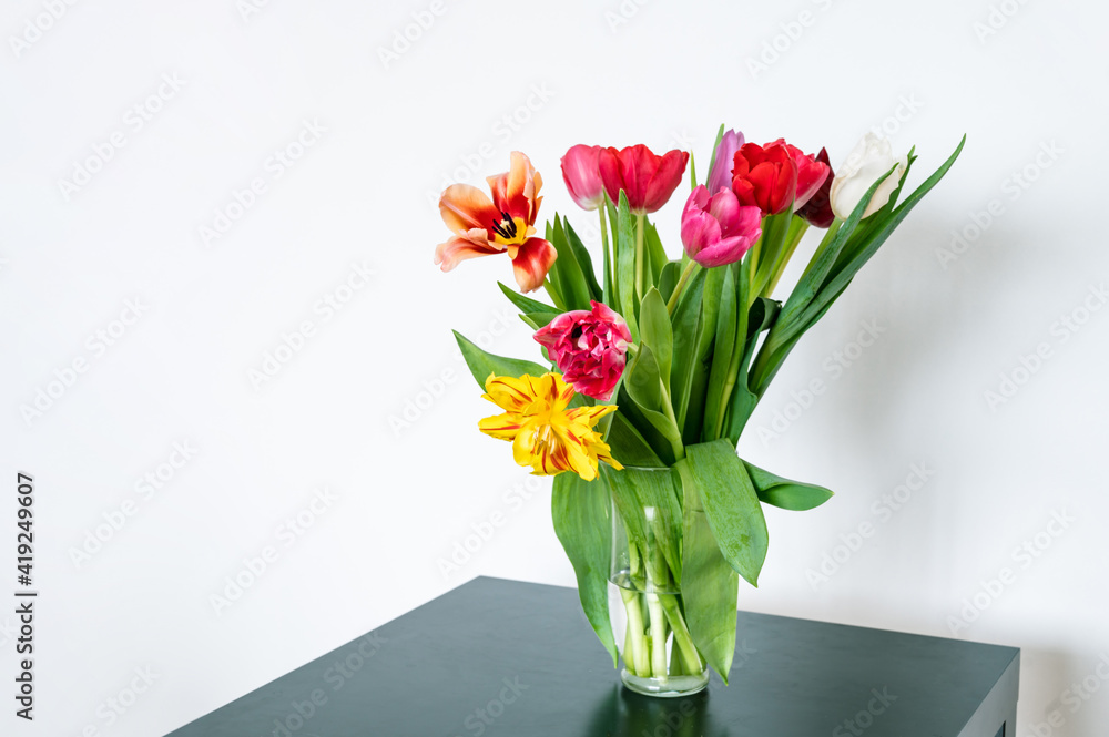 Bouquet of tulips in glass vase on black table. Beautiful spring flowers. White wall. Home decor.