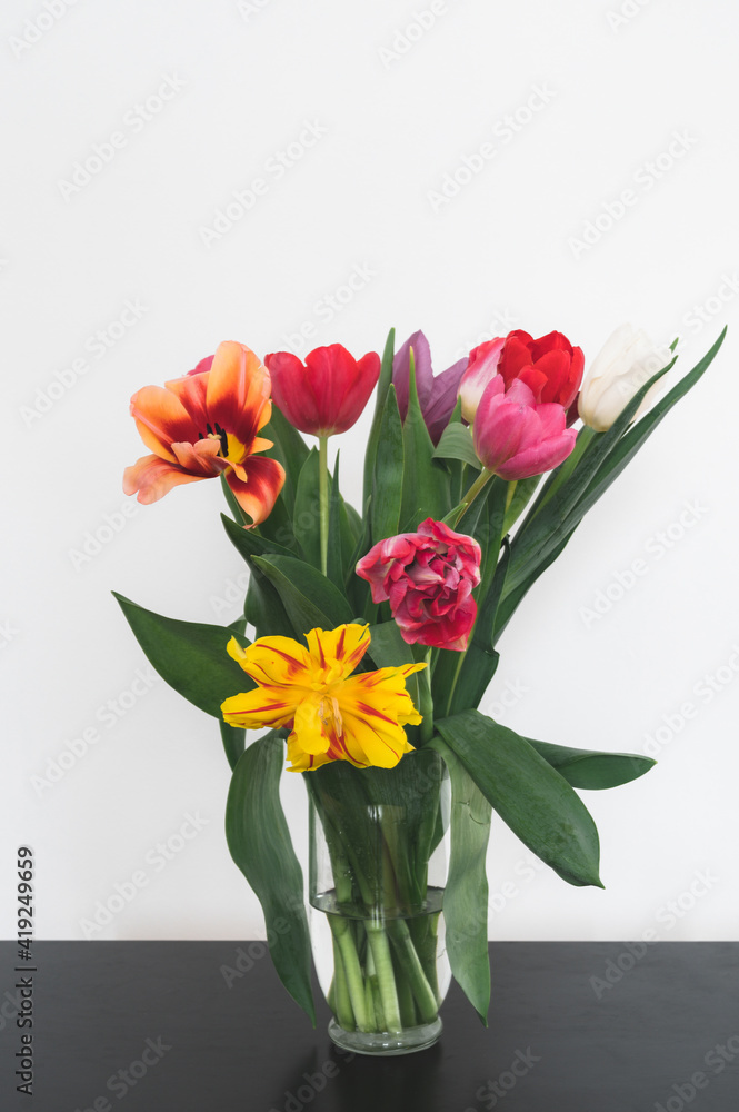 Bouquet of tulips in glass vase on black table. Beautiful spring flowers. White wall. Home decor. Bouquet of tulips in glass vase on black table. Beautiful spring flowers. White wall. Home decor.