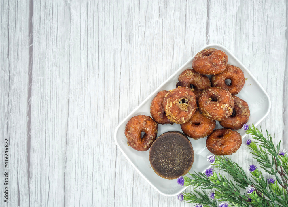 Keria gula melaka or doughnut glazed in palm sugar, made from sweet potatoes with a block of palm sugar. Selective focus points. Blurred background Keria gula melaka or doughnut glazed in palm sugar, made from sweet potatoes with a block of palm sugar. Selective focus points. Blurred background