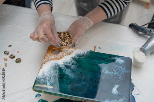 Cuadro en lienzo artist's hands decorating a wooden serving board with seashells and stones, epox