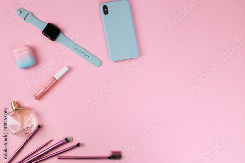 Fototapeta Naklejka Na Ścianę i Meble -  Smart gadgets on pink background. Phone, headphones, smart watch and lip gloss, perfume and makeup brushes. Top view with copy space, flat lay. Woman devices