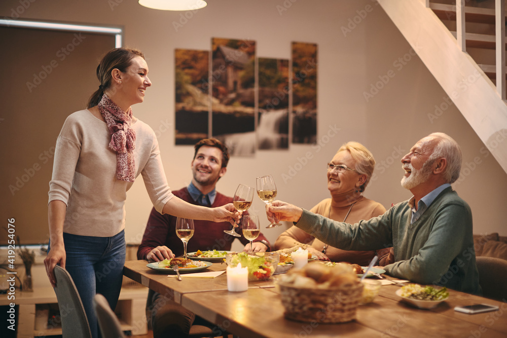 © Drazen - Happy woman toasting with her family while having dinner at dining table.