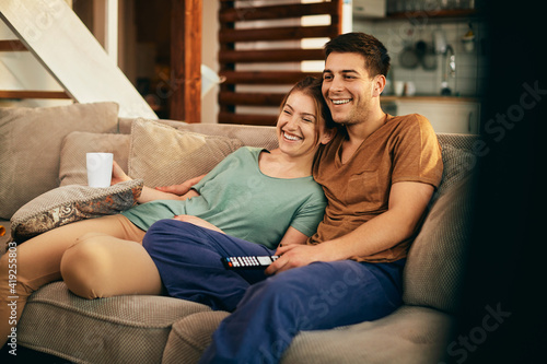 Happy couple watching Tv while relaxing on the sofa at home.