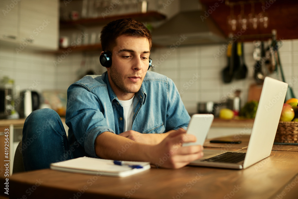 Freelance worker texting on cell phone while working on laptop at home. Freelance worker texting on cell phone while working on laptop at home.