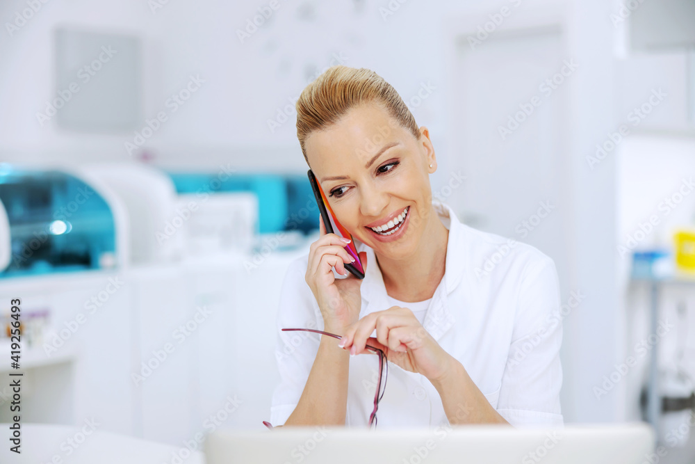 Polite attractive blond smiling lab assistant sitting in laboratory and telling good news to a patient. Polite attractive blond smiling lab assistant sitting in laboratory and telling good news to a patient.