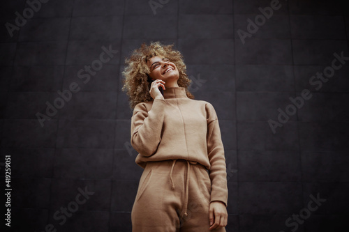 Foto Low angle view of smiling trap girl in tracksuit standing and having phone call with a friend