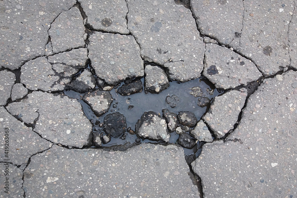 Obraz premium Large cracks on asphalt road filled with water, damage to the road surface in spring