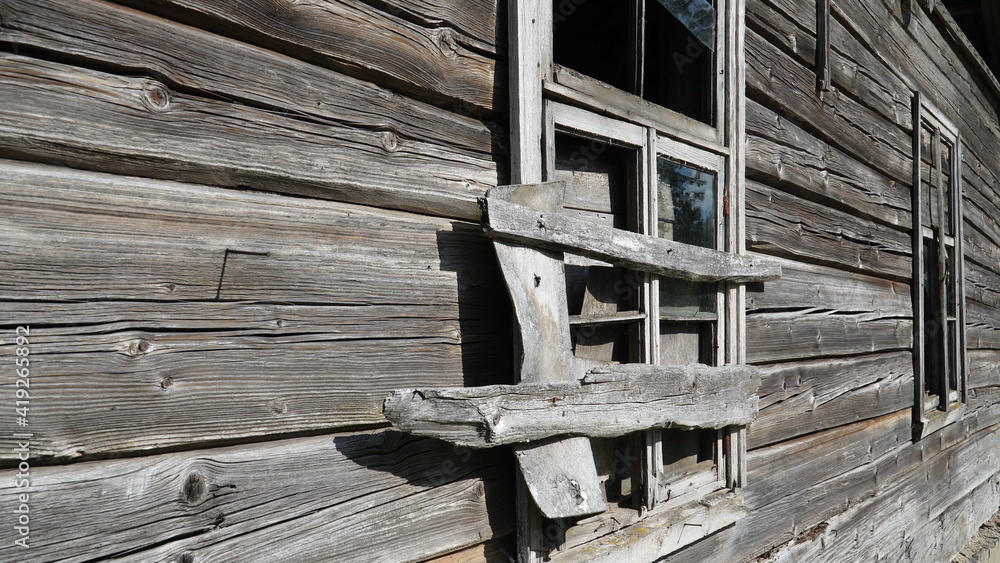 Windows of an abandoned old log house in a close-up view. The wooden building facade has faded in the sun. View to an ancient log material with cracked texture. The last century architecture.