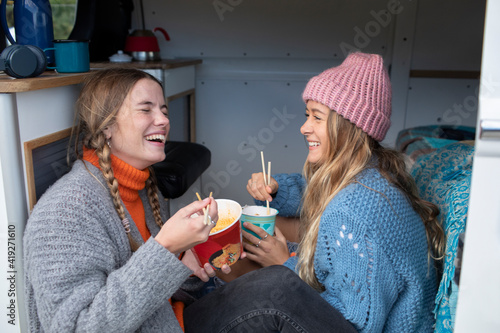 Happy young women friends eating instant noodles in camper van