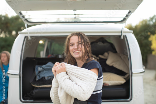 Portrait happy young woman putting on sweater outside camper van