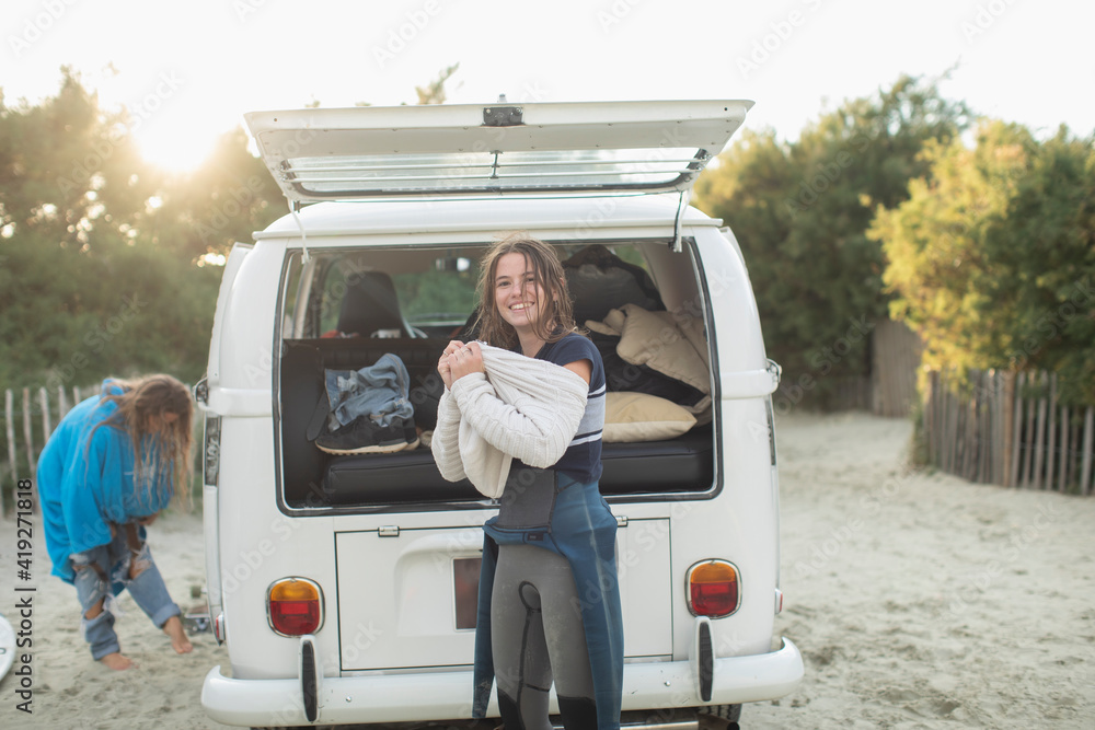 Portrait young female surfer putting on sweater at sunny camper van Portrait young female surfer putting on sweater at sunny camper van