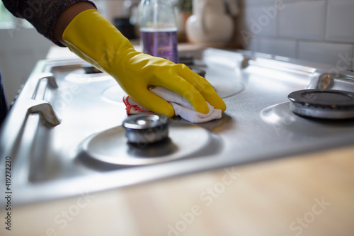 Close up woman in rubber gloves cleaning kitchen stove with rag