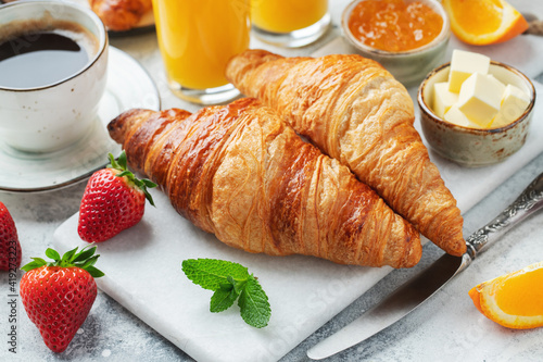 Fresh sweet croissants with butter and orange jam for breakfast. Continental breakfast on a white concrete table.