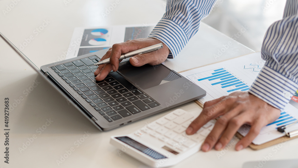 Young businessman working at home with laptop and documents on the graph, desk, close view Young businessman working at home with laptop and documents on the graph, desk, close view