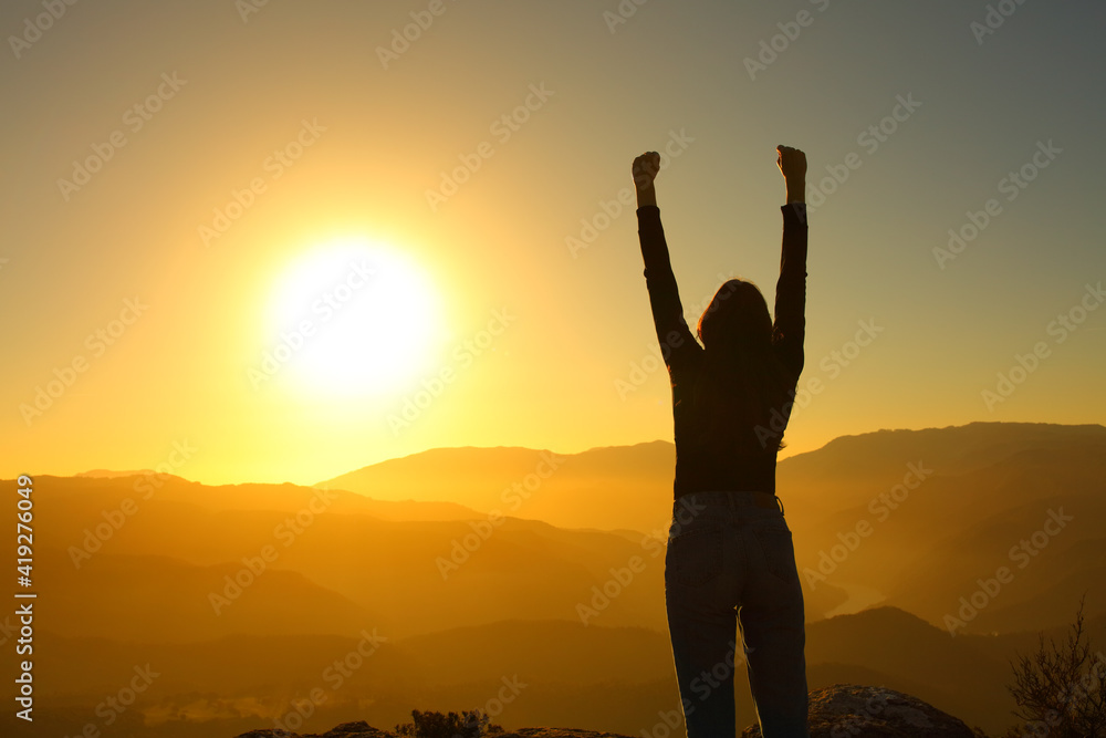 Silhouette of a woman celebrating raising arms at sunset