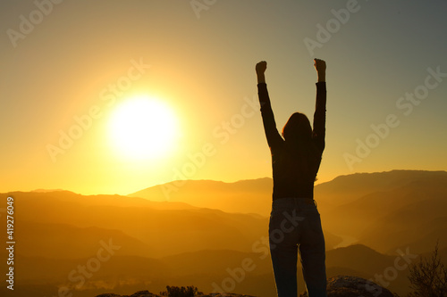 Silhouette of a woman celebrating raising arms at sunset