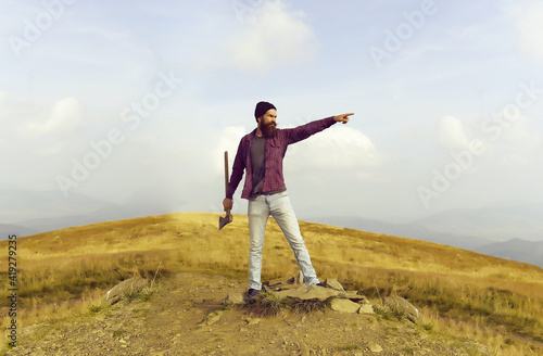 Bearded hipster man in holding axe or ax on mountain top on natural background.