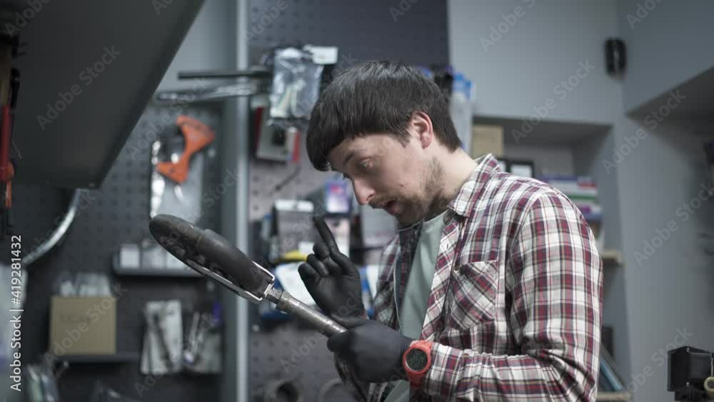 Electric scooter repair workshop. Mechanic holds in his hand broken part of child scooter and wheel. Modern environmentally friendly mode of transport. Repairman worker while working in repair shop Electric scooter repair workshop. Mechanic holds in his hand broken part of child scooter and wheel. Modern environmentally friendly mode of transport. Repairman worker while working in repair shop
