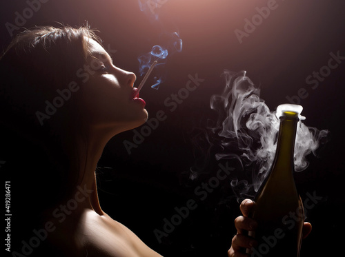 фотографія Closeup portrait of young sexy woman smoking cigarette in studio on black backgr
