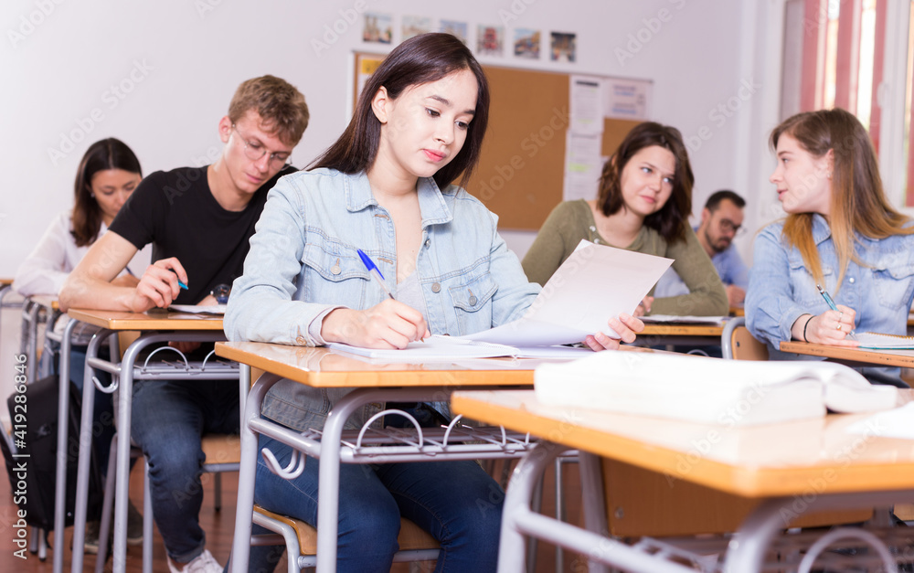 Fototapeta premium Smiling schoolgirl is learning and answering the question on paper in the class.