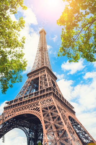 Eiffel Tower against the sky with green trees in Paris, France. Famous travel destination.