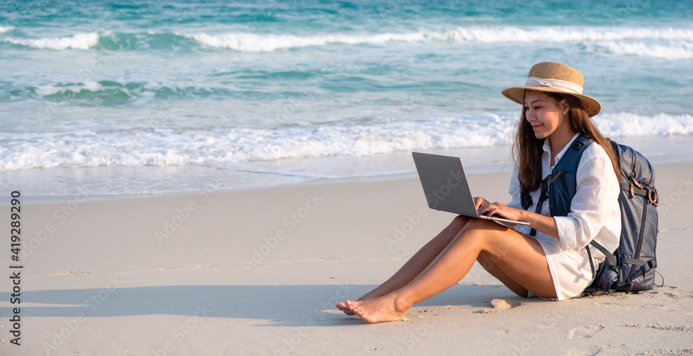 A female traveler using and working on laptop computer while sitting on the beach