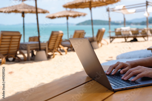 Closeup of a woman working and typing on laptop computer on the beach photo