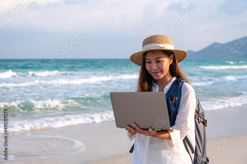 A young female traveler using and working on laptop computer while walking on the beach
