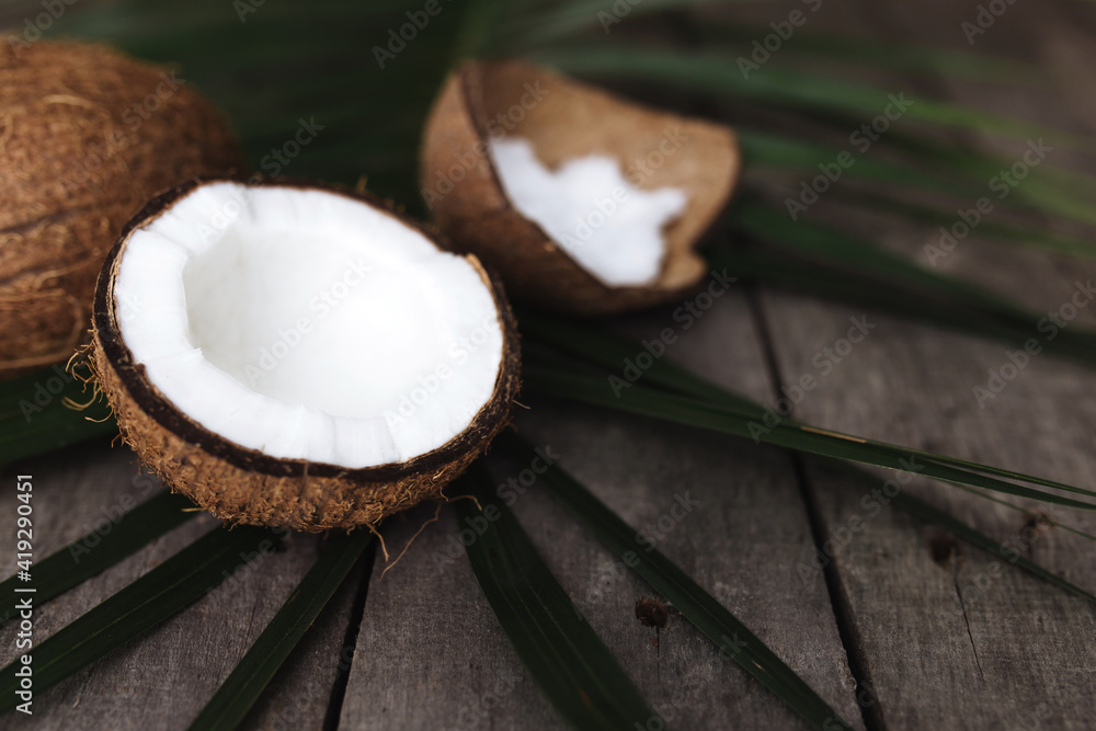 Broken coconuts on gray wooden background with palm leaf. White coconut pulp