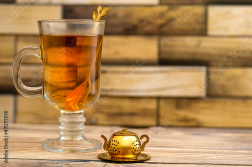 Vintage tea strainer and a glass of tea on a wooden table with place for text. Teapot-shaped golden tea strainer